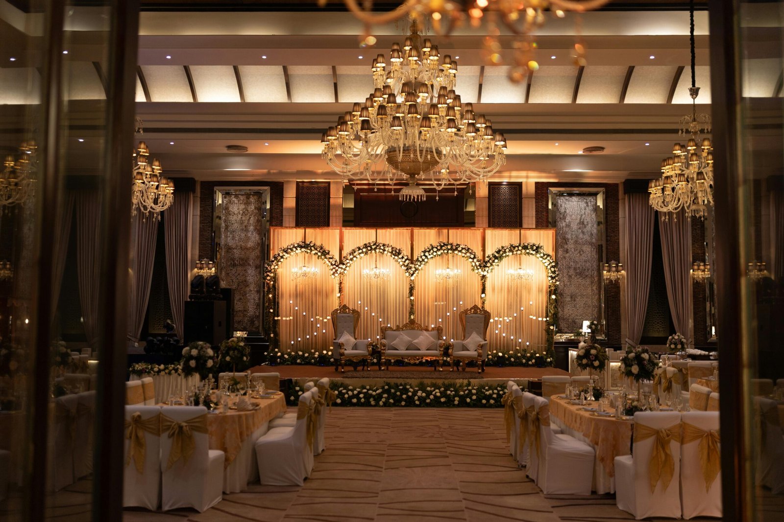 Luxurious wedding hall decorated with chandeliers and floral arrangements for an elegant celebration.